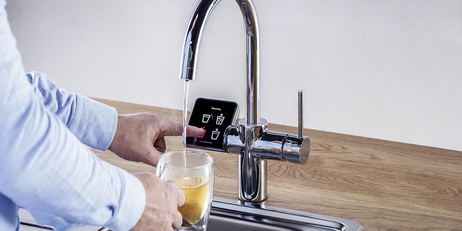 Ein Mann der heisses Wasser aus dem Trinkwasserhahn in eine Tasse laufen laesst