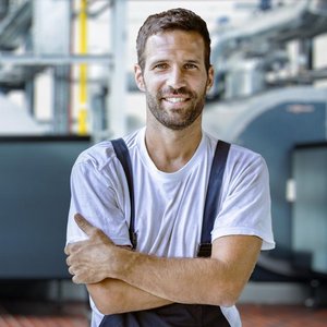 Ein lächelnder Mann in Arbeitskleidung mit verschänkten Armen