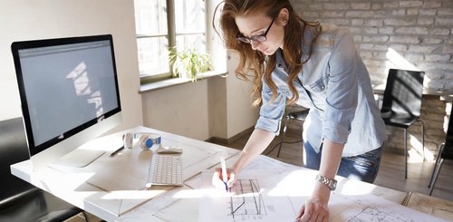 Eine Frau steht an einem Bürotisch und makiert eine Technische Zeichnung